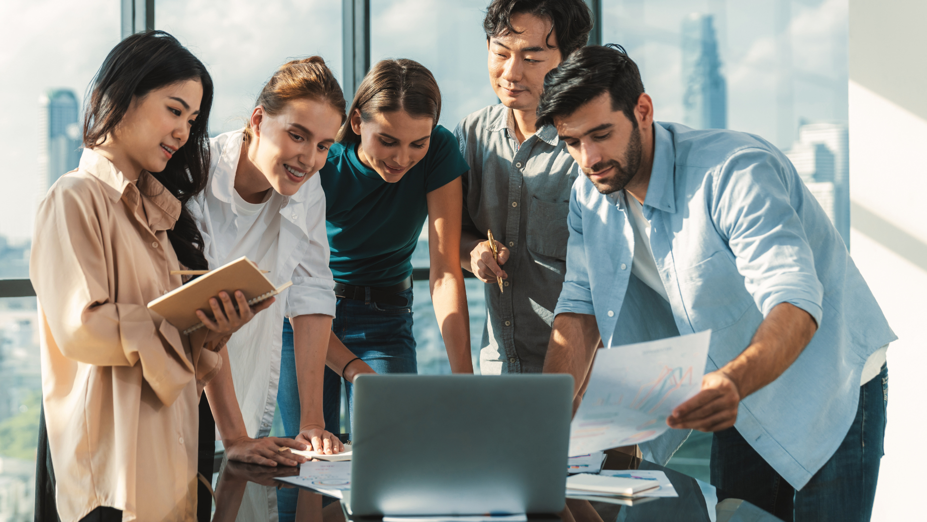 A diverse team of professionals collaborating around a laptop, reviewing documents and discussing strategies, representing the collaborative approach of Integris Group Services to deliver customer-centric solutions.