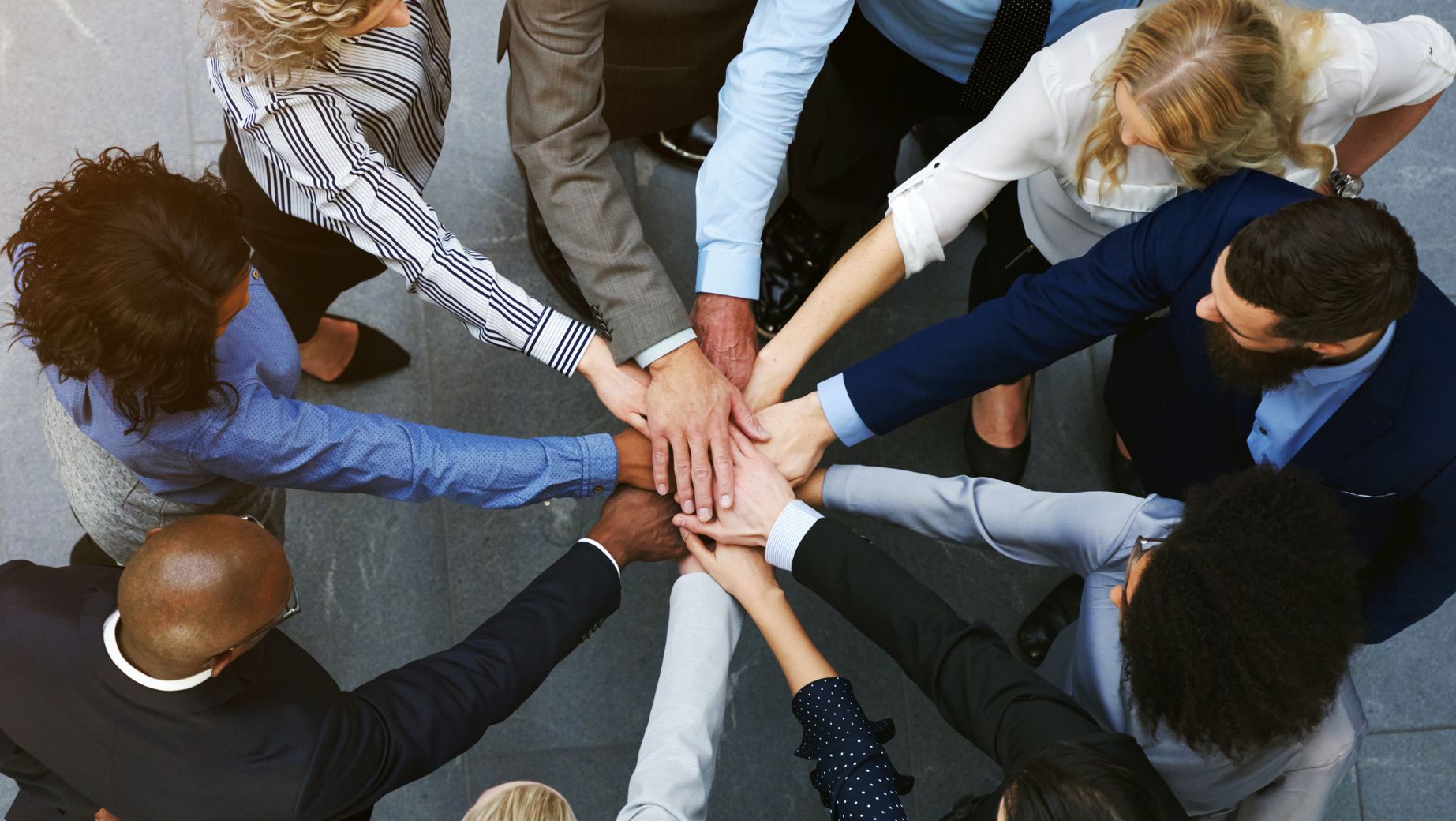 A diverse group of professionals standing in a circle with their hands joined together, symbolizing unity, collaboration, and shared accountability.